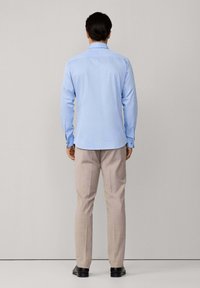 Camicia azzurro chiaro a maniche lunghe con colletto, polsini abbottonati e orlo curvo; abbinata a pantaloni beige e scarpe nere.