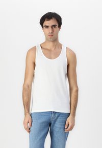 Fehér pamut ujjatlan felső széles vállpántokkal, kerek nyakkivágással és laza szabással, amelyet a megfakult kék denim farmernadrággal párosítanak.