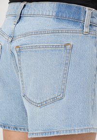 Pantalones cortos de mezclilla en un tono claro con un dobladillo deshilachado. Cuenta con dos bolsillos traseros y costura en contraste. Textura suave con un ajuste casual.