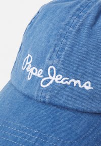 Zila denim beisbola cepure ar redzamām šuvēm, izliekts noslēgums un izšūts "Pepe Jeans" logo baltā krāsā priekšpusē.