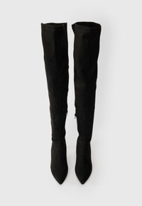 Mustad üle põlve saabased, mis on valmistatud seemisnahast, terava varbaga ja saleda siluetiga. Sisaldab reguleeritavaid külgzippe sobivuse tagamiseks.