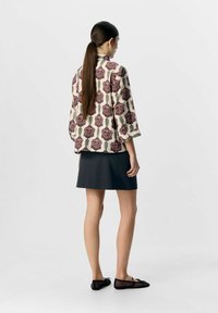 Bluse mit Blumenmuster und 3/4-Ärmeln, beiger Hintergrund, dunkelrosa Rosen, kombiniert mit einem dunkelgrauen Rock und schwarzen Ballerinas aus Netz.