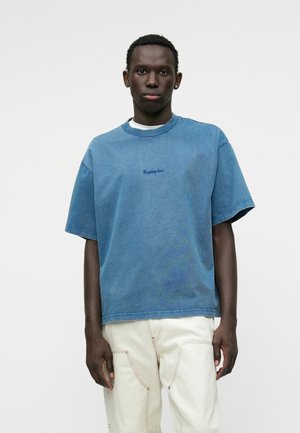 Camicia in denim a maniche corte di colore azzurro chiaro, con colletto girocollo a costine e logo ricamato 'Replay Inc.' di colore blu scuro. Vestibilità rilassata.