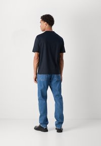 T-shirt marine à manches courtes et encolure ras du cou, associé à un jean bleu. Le tissu semble lisse, avec une coupe décontractée et sans motifs visibles.