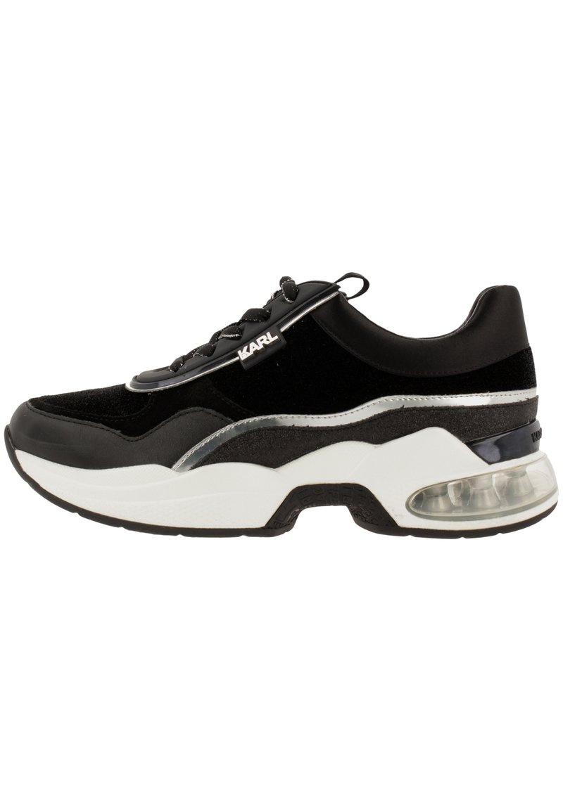 Baskets athlétiques noires avec dessus en suède et synthétique, semelle en caoutchouc blanche, accents argentés et coussin d'air visible au talon.