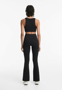 Zwarte sportcrop top met brede banden, gecombineerd met hooggeografische, uitlopende legging, beide gemaakt van een textiele, rekbare stof.
