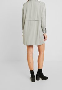 Grön satin klänning med långa ärmar, hög krage och en bakre yoke-söm; bärs med svarta ankelstövlar med klack.