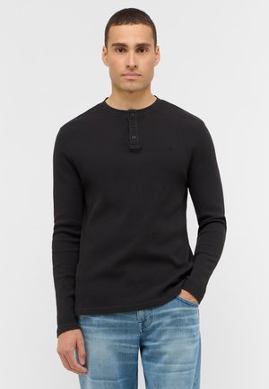 Black long-sleeve henley shirt with a ribbed texture, three-button placket, and crew neckline, paired with light blue denim jeans.