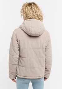 Beżowa kurtka z korduroyu z kapturem, pikowany design i boczne kieszenie. Posiada prążkowaną teksturę oraz haftowane logo na rękawie.