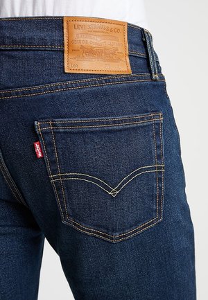 Poche arrière et zone de la taille d'un jean Levi's bleu foncé avec un patch en cuir de la marque et une étiquette Levi's rouge sur la poche.