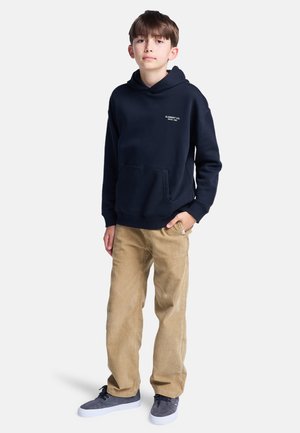 Sudadera navy con bolsillo frontal y texto de logo en blanco, combinada con pantalones de pana color beige y zapatillas grises. Atuendo sencillo y casual.