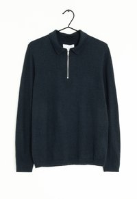 Marinefarbener Pullover mit langen Ärmeln, einem Kragen und einem halben Reißverschluss. Hergestellt aus weichem Material mit glatter Textur. Hängt an einem schwarzen Haken.