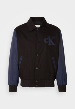 Black jacket with navy sleeves, button closure, and embroidered "cK" logo. Features a collared neck and elasticized cuffs for a fitted look.