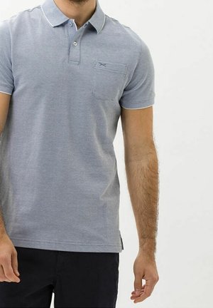 Homme portant un polo à manches courtes gris clair avec une poche poitrine et un pantalon noir, visible du cou aux hanches.