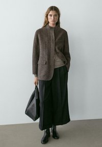 Brown wool-blend jacket with a stand collar, single button closure, front pocket, paired with wide black trousers and black leather bag.