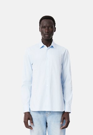 Camisa de manga larga azul claro con cuello abotonado, presenta rayas verticales blancas y un logo bordado en el pecho. Material de algodón.