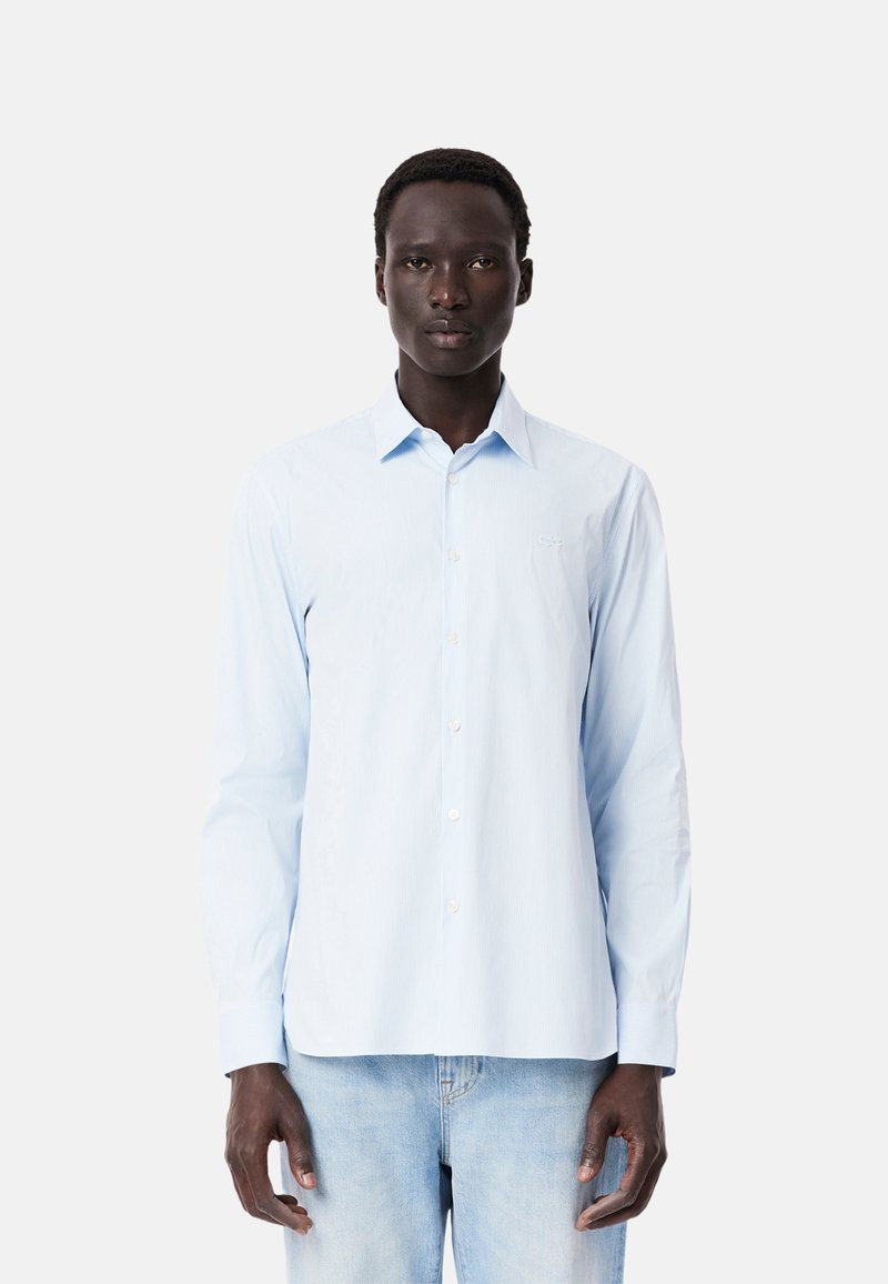 Camisa de manga larga azul claro con cuello abotonado, presenta rayas verticales blancas y un logo bordado en el pecho. Material de algodón.