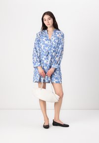 Rochie ușoară albastră cu un model floral, avea un închizător cu nasturi în față și o talie reglabilă. Asortată cu o geantă albă și balerini negri.