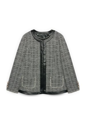 Schwarze und weiße Tweedjacke für Damen mit Kunstlederbesatz, zwei Fronttaschen und Perlenknöpfen an den Ärmeln.