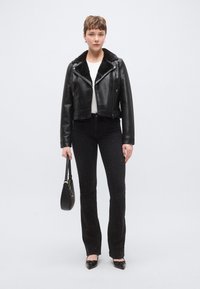 Fekete bőr rövidített dzseki műszőrme gallérral, fekete farmerrel, amely ezüst pöttyökkel díszített. A modell egy kis fekete kézitáskát tart.