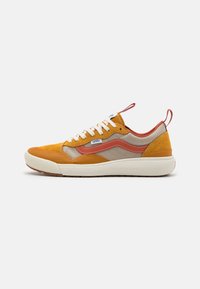 Låga Vans-sneakers med senapsgul mocka, beige tyg, bränd orange rand, vita skosnören och vit strukturerad sula, sidovy på vit bakgrund.