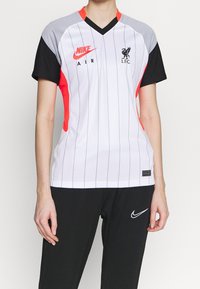 Damska koszulka Nike z białą podstawą, pionowymi czarnymi paskami, czerwonymi akcentami, szarymi ramionami oraz logo Liverpool FC na lewej piersi.