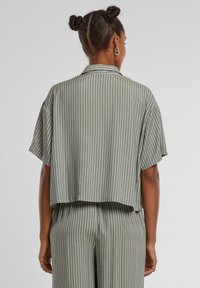 Cropped, short-sleeve shirt in light green, featuring vertical white stripes and a notched collar, made from smooth fabric.
