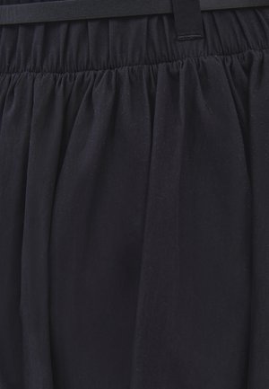 Cintura de falda negra con tela fruncida, pasadores de cinturón cosidos y pliegues, mostrando la textura y caída del material.