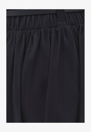 Cintura de falda negra con tela fruncida, pasadores de cinturón cosidos y pliegues, mostrando la textura y caída del material.