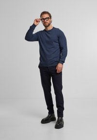 Maglione blu navy in un materiale morbido, maniche lunghe. Pantaloni neri, stivali robusti con suola spessa. Presenta una vestibilità rilassata e un design moderno.