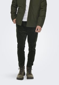 Green padded jacket, white t-shirt, dark green corduroy pants, and olive-green boots with black laces and textured soles.