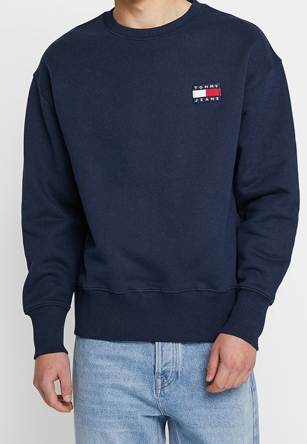 Sweat-shirt bleu marine à col rond avec petit logo Tommy Jeans sur la poitrine, porté avec un jean en denim bleu clair.