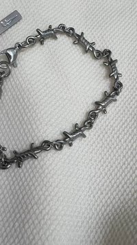 Pulseira de prata com um design de corrente e elementos de arame farpado. Superfície de metal lisa com fecho de lagosta e etiqueta de logo.