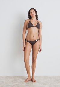 Brown bikini with a triangular top and matching low-rise bottom. Features adjustable straps and metal accents on the side. Smooth texture.