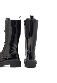 Mustad nahkadega põlve kõrgused saapad, paksu kummist põhjaga, millel on lipsudega esiosa ja külgmine tõmblukk mugavaks selga panemiseks.