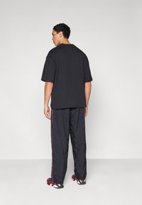 Μαύρο υπερμεγέθες μπλουζάκι, casual εφαρμογή, σετ με χαλαρά σκουρόχρωμα μπλε παντελόνια με κόκκινες ρίγες στο πλάι, ολοκληρωμένο με παπούτσια σε μαύρο και κόκκινο μοτίβο.