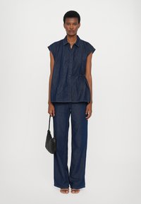 Camisa de ganga com mangas curtas e botões, combinada com calças de ganga de perna larga, ambas em azul escuro. Apresenta uma cintura ajustada e uma bolsa preta.