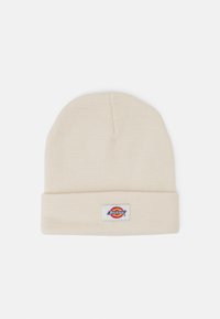 Cream knit beanie with a folded cuff and a rectangular label featuring a multi-colored logo. Soft texture and classic design.