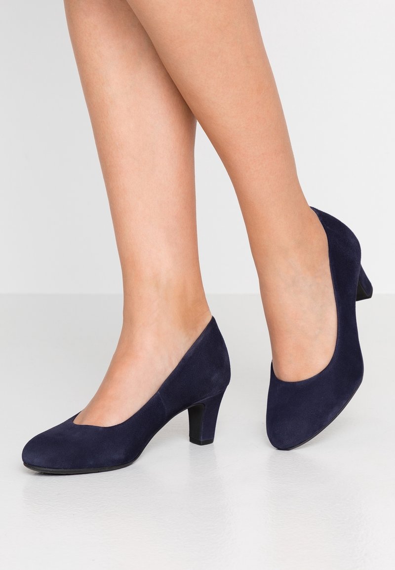 Escarpins en suede bleu marine avec un bout arrondi et un petit talon bloc, présentant un design découpé et une texture lisse.