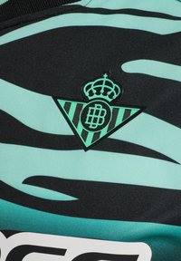 Camiseta deportiva negra y verde menta que presenta un logo triangular texturizado con una corona y un patrón de rayas en la tela.