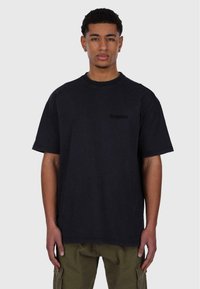 Schwarzes, übergroßes T-Shirt mit kurzen Ärmeln aus Baumwolle, das auf der Vorderseite ein dezentes Logo aufweist, mit rundem Halsausschnitt und lockerer Passform.