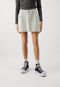 Jupe mini rayée en tissu léger avec une taille solide, dotée de deux poches latérales et d'une fermeture à boutons, associée à des baskets montantes noires.