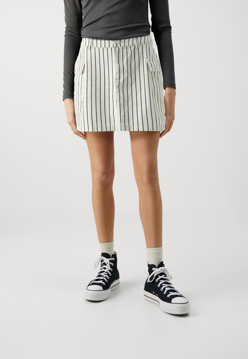 Jupe mini rayée en tissu léger avec une taille solide, dotée de deux poches latérales et d'une fermeture à boutons, associée à des baskets montantes noires.