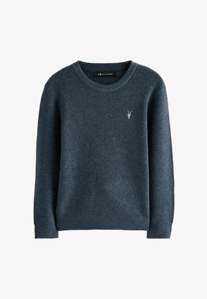 Tamsiai mėlynas megztinis su apvalia iškirpte, šonkaulinio tekstūros, ilgomis rankovėmis ir mažuoju siuvinėtų emblema ant krūtinės.