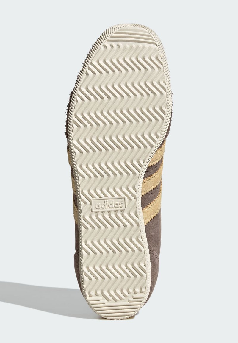 Brun sula i mocka för sneakers med zickzack-mönster, beige accenter och präglad logotyp. Har en klassisk sportskosilhuett.