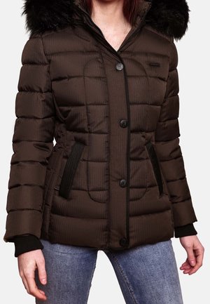 Femme portant une veste d'hiver matelassée marron foncé avec une capuche en fourrure noire et des boutons noirs, associée à un jean bleu.