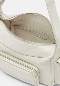 Borsa a mano in pelle color beige chiaro con una texture liscia. Dotata di un compartimento principale con zip, tasca frontale e scomparti per carte all'interno.