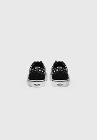 Mustad mustad kingad valgete kummist talladega, millel on dekoratiivsed kuldsed nupud kontsade ja külgede peal. Klassikaline Vans'i logo taga.