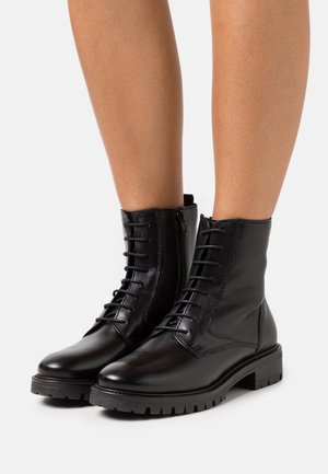 Botas de tobillo de cuero negro con un acabado liso, cordones en la parte delantera, cremallera lateral y suela resistente. Presentan detalles de costura y una puntera redonda.