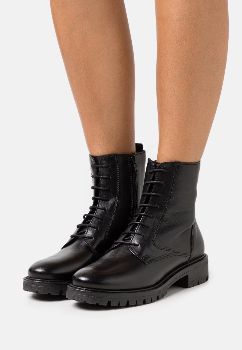 Stivali alla caviglia in pelle nera con finitura liscia, alla moda con lacci sul davanti, zip laterale e suola robusta. Presentano dettagli cuciti e punta tonda.